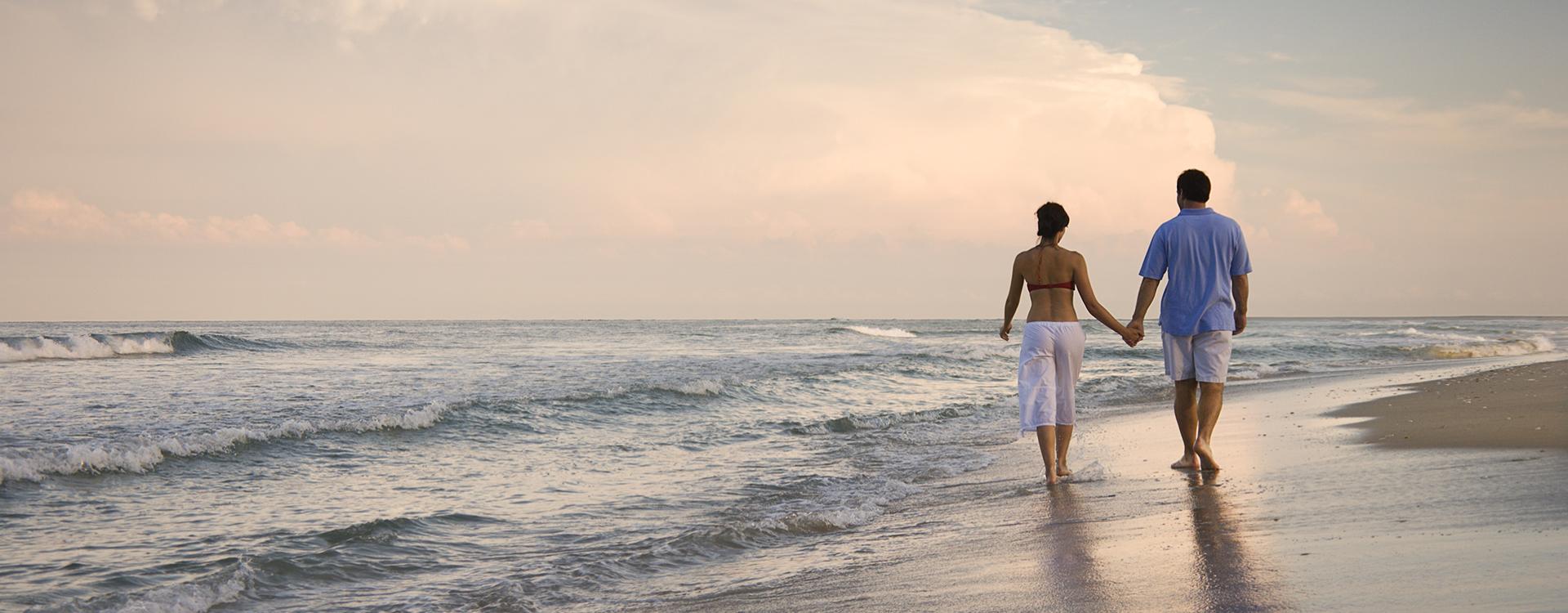 Coppia cammina mano nella mano sulla spiaggia al tramonto.