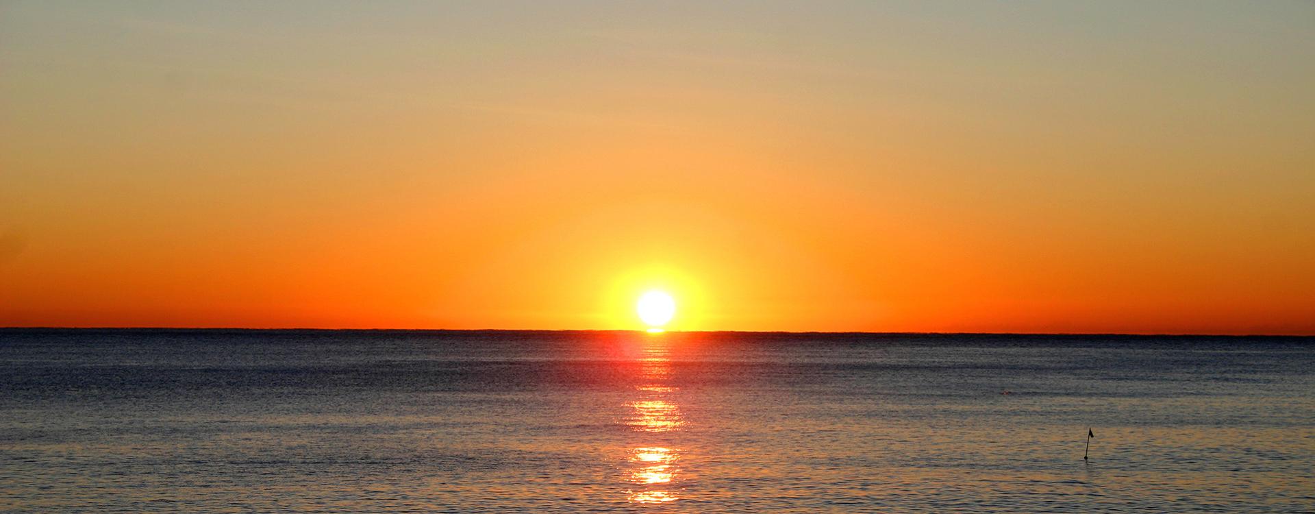 Tramonto sul mare con riflessi dorati e cielo arancione.