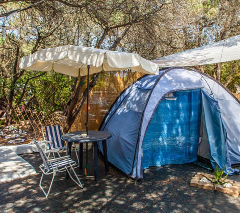 Tenda da campeggio con ombrellone e sedie, immersa nella natura ombreggiata.